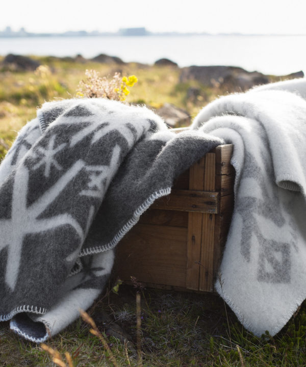 Bind rune blankets in pale and dark greys styled on a wooden crate with the Icelandic countryside as a backdrop.