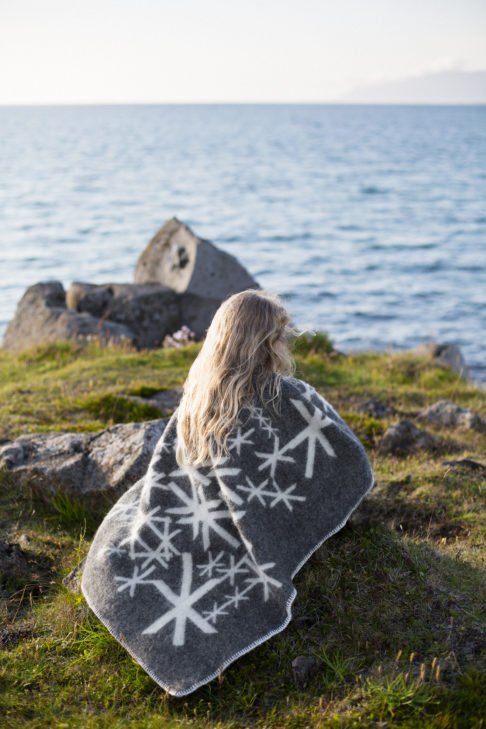 Grey blanket throw depicting Nordic bind runes meaning strength, wrapped around a girl sitting by the sea.