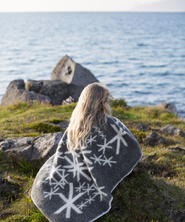 Grey blanket throw depicting Nordic bind runes meaning strength, wrapped around a girl sitting by the sea.