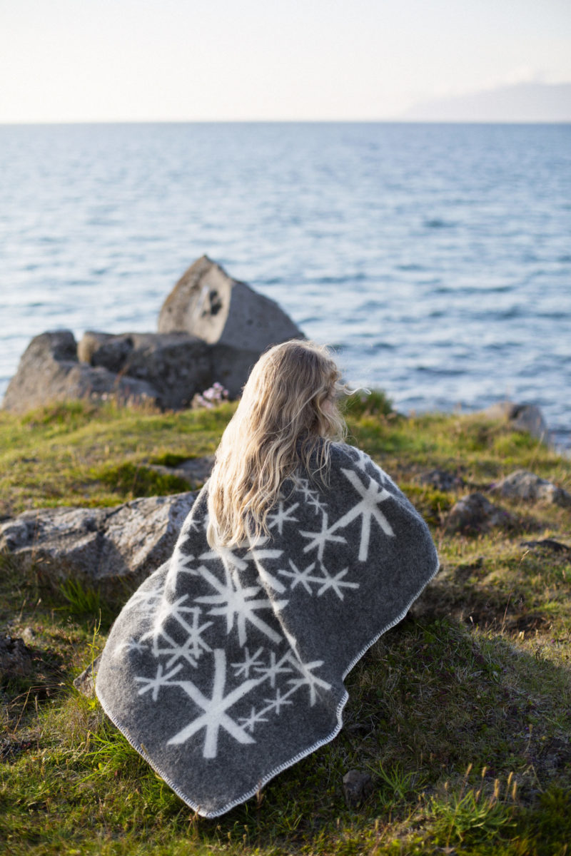 Grey blanket throw depicting Nordic bind runes meaning strength, wrapped around a girl sitting by the sea.