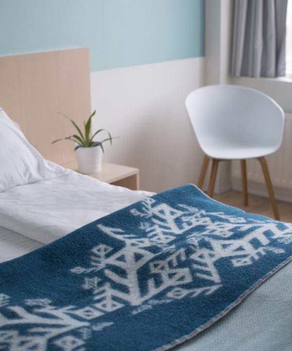 Folded teal blanket throw depicting Nordic bind runes symbolising love, on a bed.