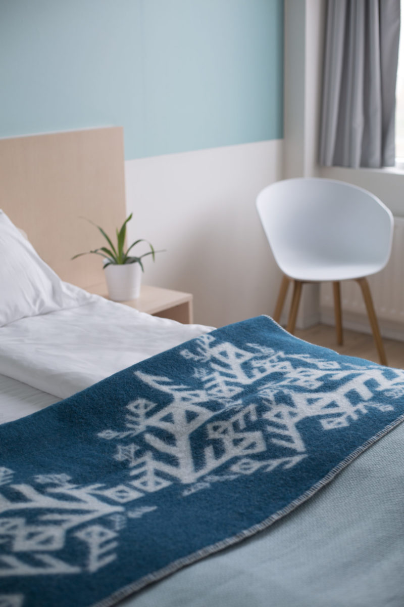 Folded teal blanket throw depicting Nordic bind runes symbolising love, on a bed.