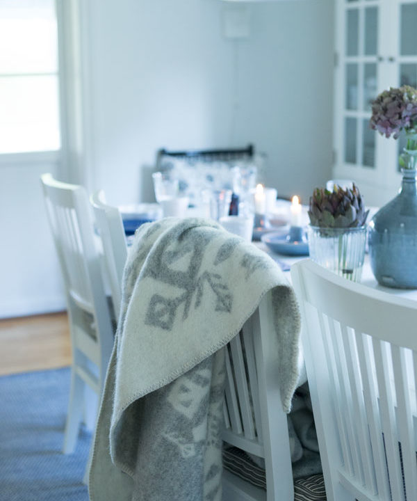 A pale grey Icelandic bind rune blanket on the back of a dining chair in a Scandinavian feel dining room setting.