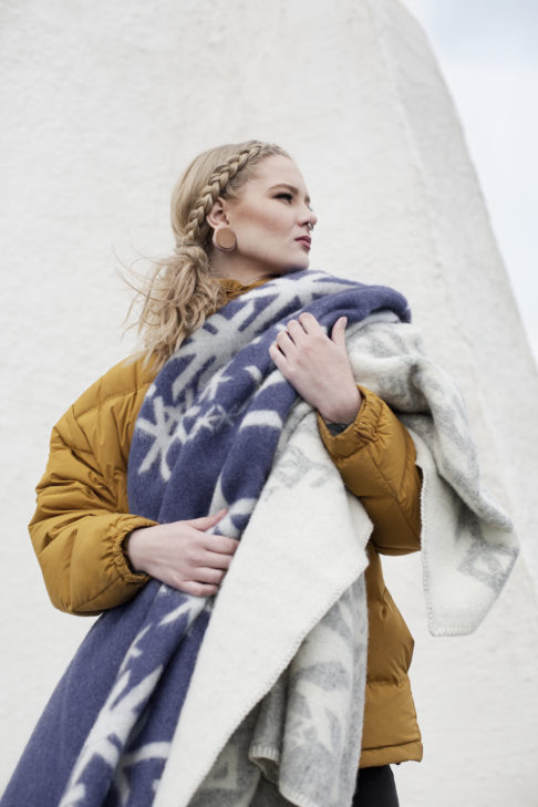 A navy blue blanket throw with ancient Norse symbolism bind runes design, held by a model.