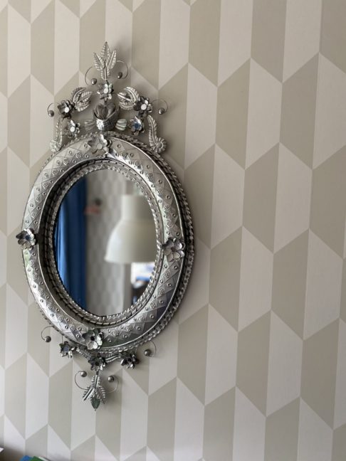 A Mexican tin art mirror hung against subtle, geometric modern wallpaper.