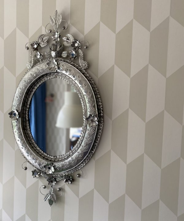 A Mexican tin art mirror hung against subtle, geometric modern wallpaper.