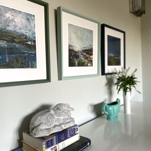 Northern Ireland prints hung in a row and framed in toning shades of green and blue above a sideboard.