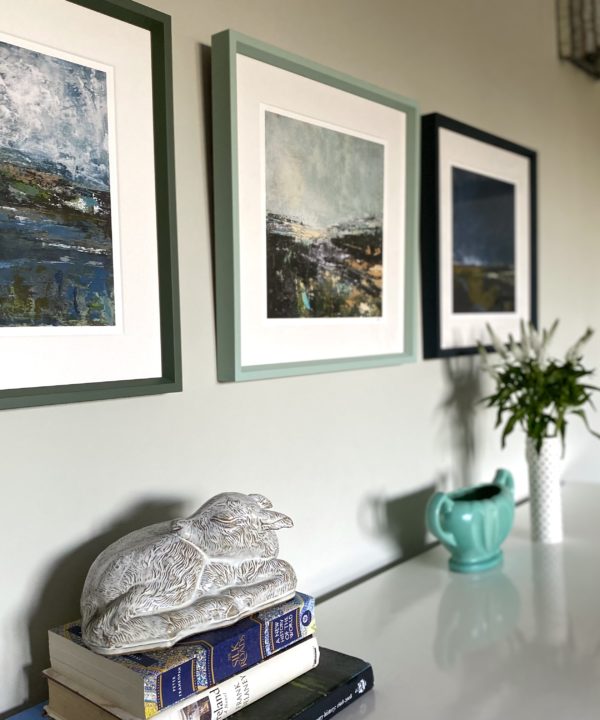 Northern Ireland prints hung in a row and framed in toning shades of green and blue above a sideboard.