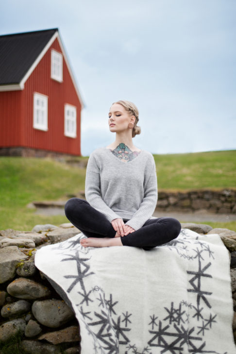 Grey reversible blanket throw with Nordic bindrunes under a model against a red, wooden panelled shed.