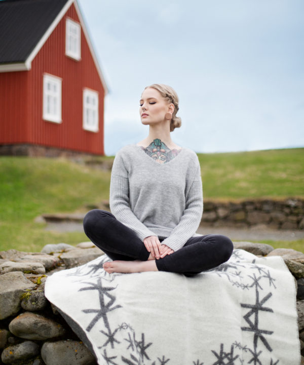 Grey reversible blanket throw with Nordic bindrunes under a model against a red, wooden panelled shed.