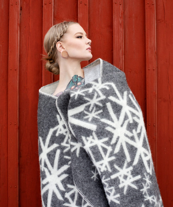 Grey blanket throw with Nordic bindrunes on a model against a red, wooden panelled shed.