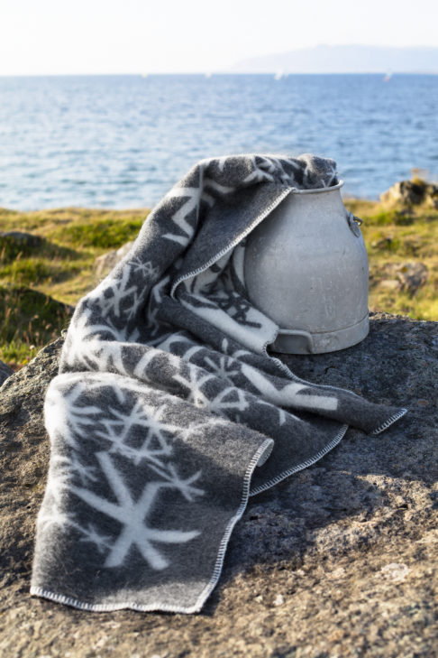 Grey blanket throw with Nordic bind runes styled on a vintage milk pail with the Icelandic countryside as a backdrop.