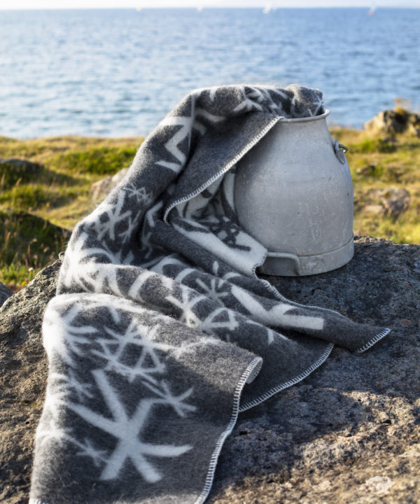 Grey blanket throw with Nordic bind runes styled on a vintage milk pail with the Icelandic countryside as a backdrop.