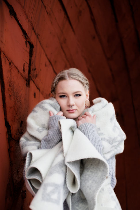 A model wrapped up in our light grey blanket throw with Nordic bindrune symbols that reference love.