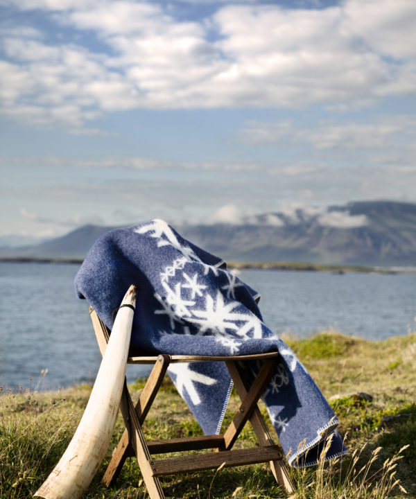 An Icelandic runes motif blanket in blue styled in the Icelandic countryside with sea and mountains as a backdrop.