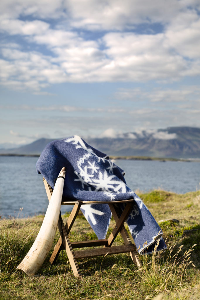 An Icelandic runes motif blanket in blue styled in the Icelandic countryside with sea and mountains as a backdrop.