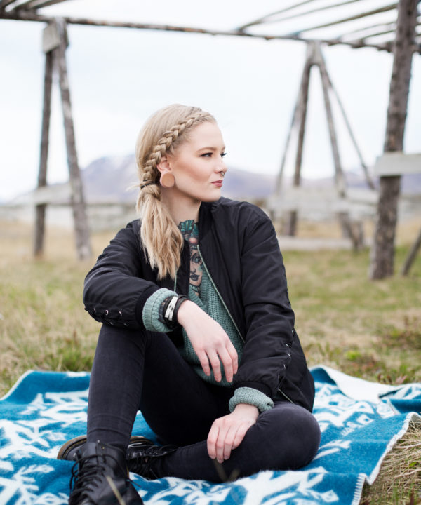 A model sitting on a teal blanket throw in the Icelandic countryside.