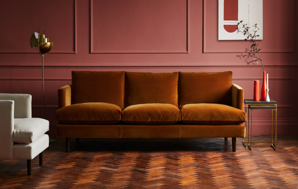 A rust-coloured velvet adorns this smart sofa from Arlo & Jacob in a panelled room with parquet flooring.