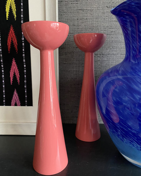 Pink candle holders in gloss Coral with a sleek, Scandi-style, retro shape against a grey modern backdrop.