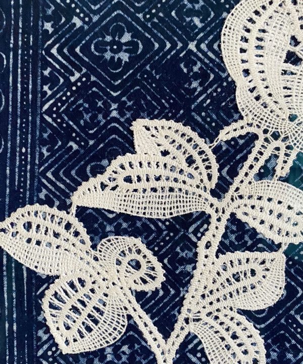 Textile art close up shot of a bobbin lace rose framed against indigo textiles.