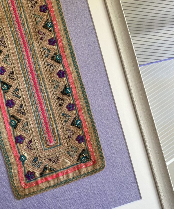 Detail of a vintage, beaded, Thai framed textile with a pale lilac backdrop.