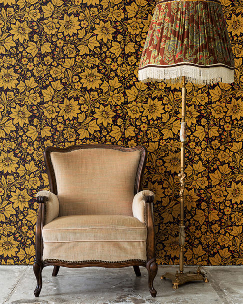 A vintage chair and lampshade with Russian folk art wallpaper in gold as the backdrop.