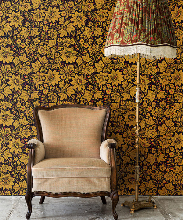 A vintage chair and lampshade with Russian folk art wallpaper in gold as the backdrop.