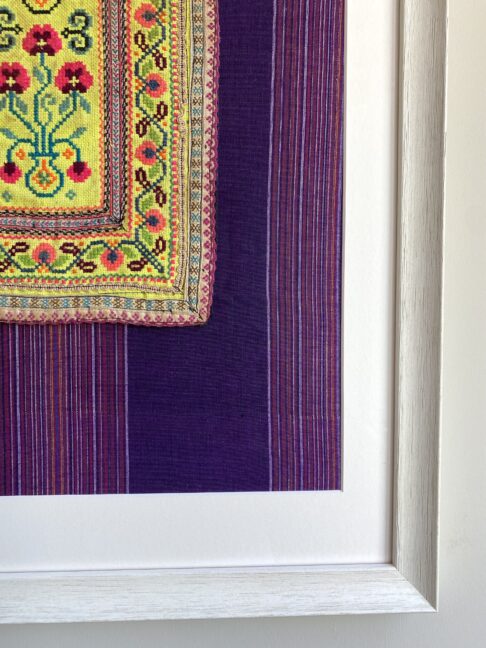 Detail of a framed Thai textile panel against purple striped cotton.