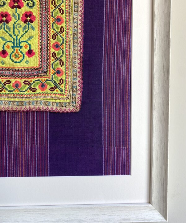 Detail of a framed Thai textile panel against purple striped cotton.