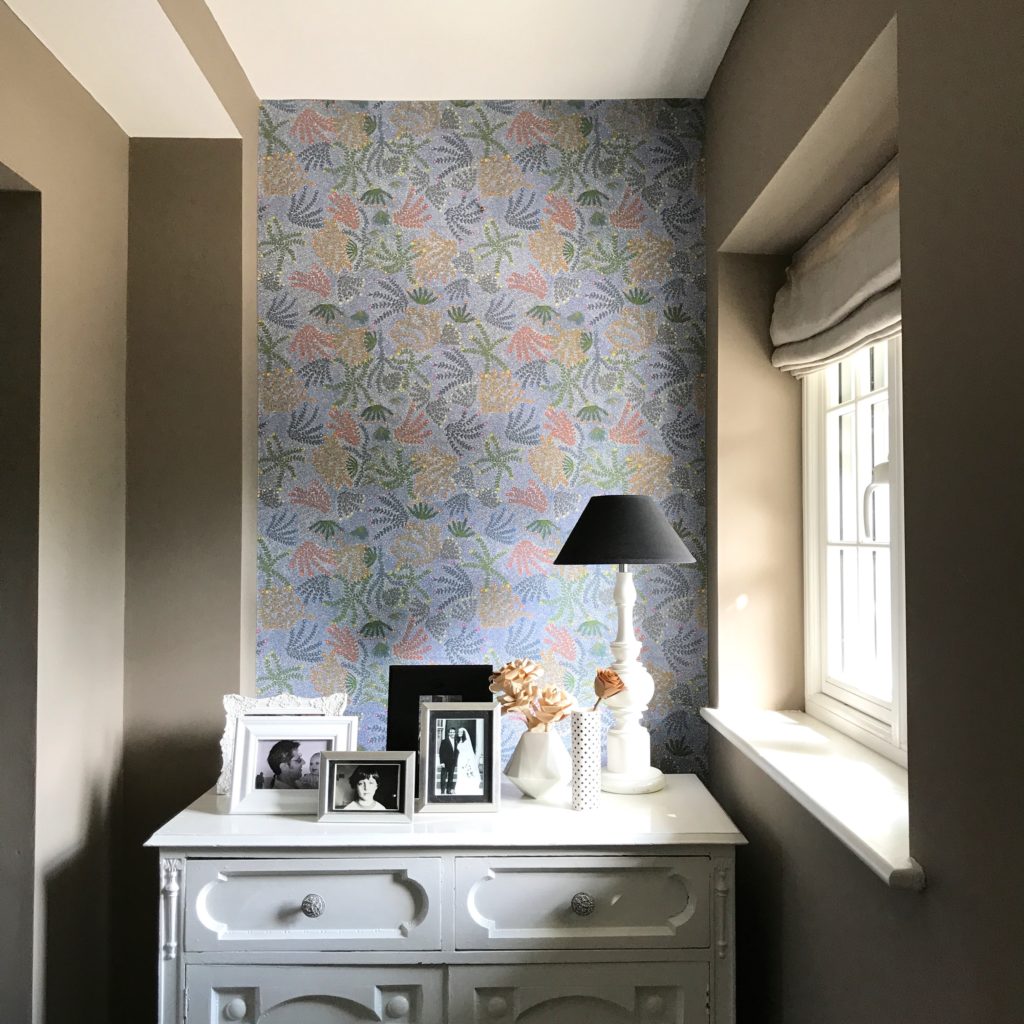 A hallway displaying indigenous Aboriginal art wallpaper above a vintage sideboard in white.