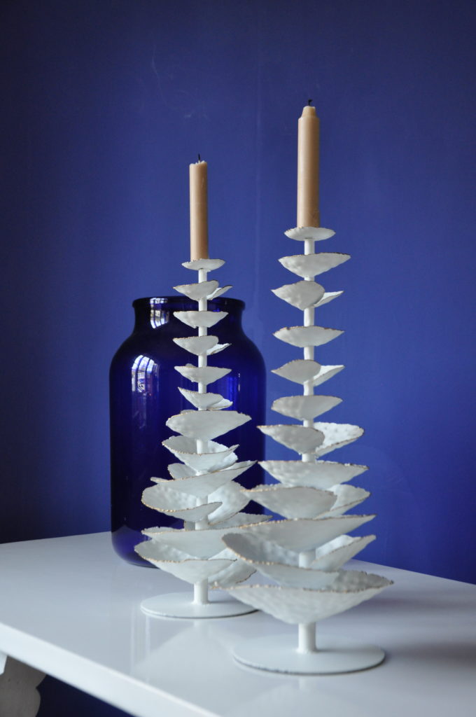 Two elegant, white metalwork candlesticks against a blue backdrop.