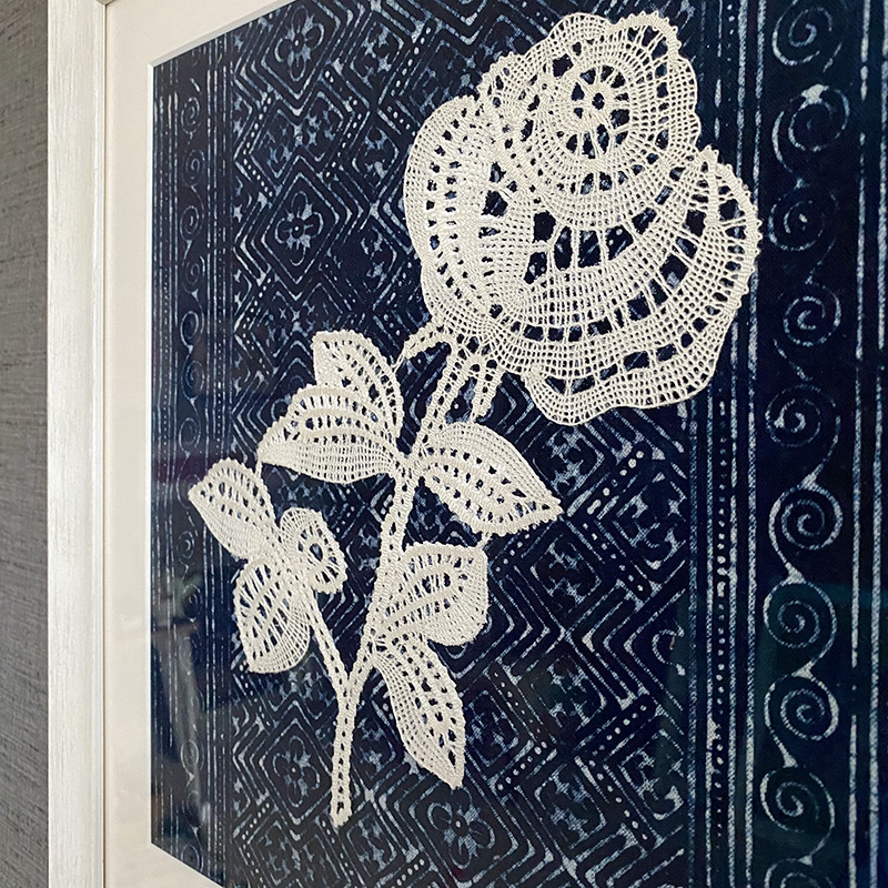 Detail of a framed bobbin lace rose, handmade in Croatia, framed in white wood, against hand-dyed indigo cloth from Thailand.