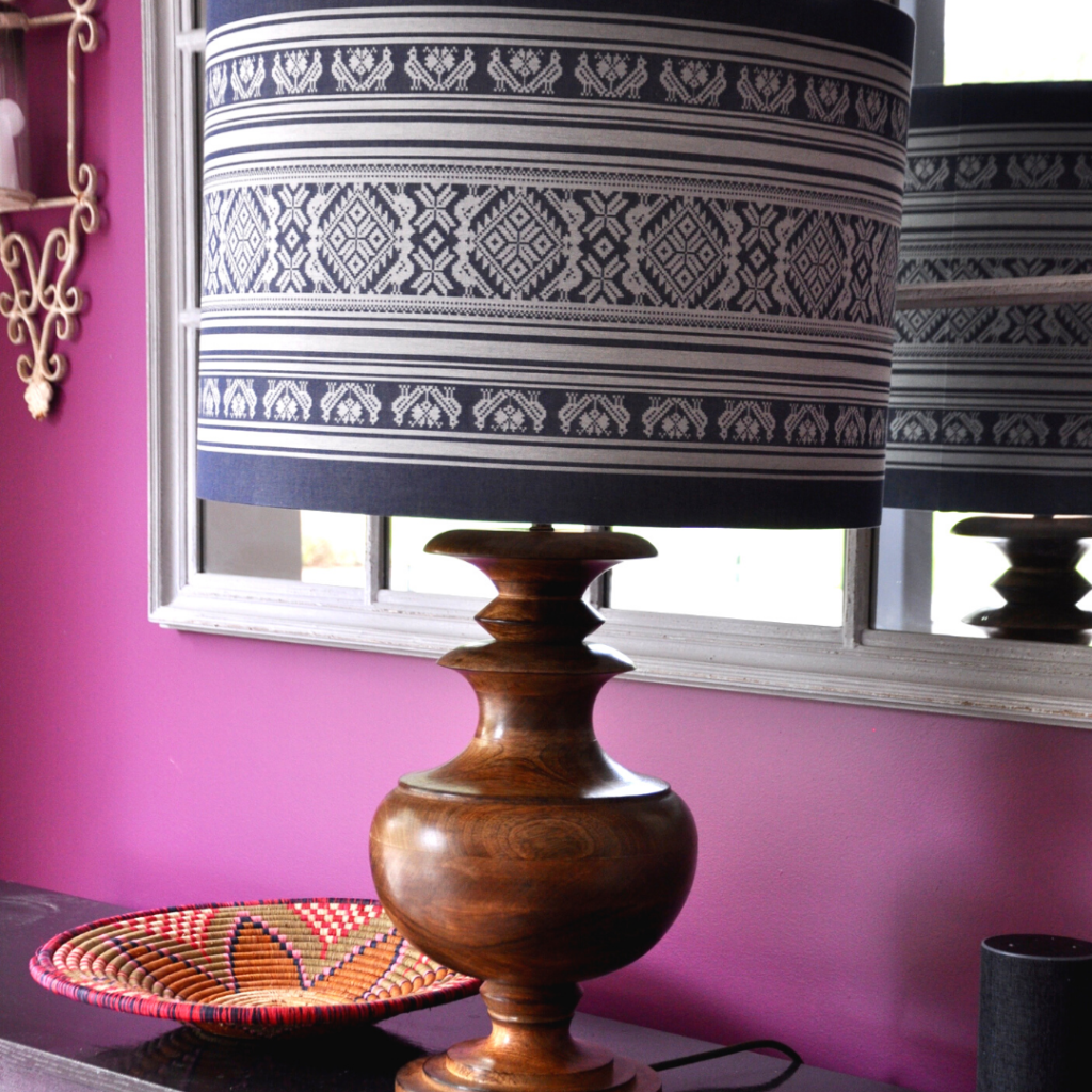 A Hungarian pattern drum lampshade on a wooden base against magenta pink walls.