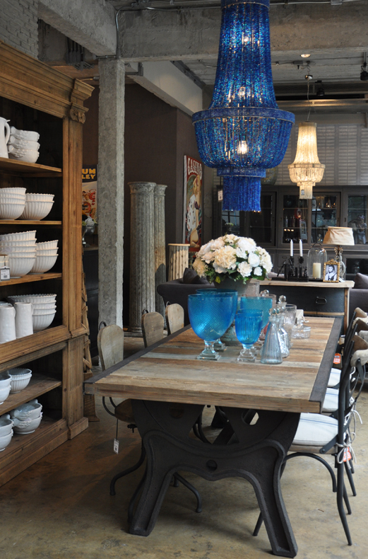 A stylish, vintage-inspired dining table in an urban loft space with a striking blue glass chandelier.