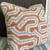 A hand print fabric burnt orange cushion with soft blue accents in a Moorish-inspired, maze-like design on linen.