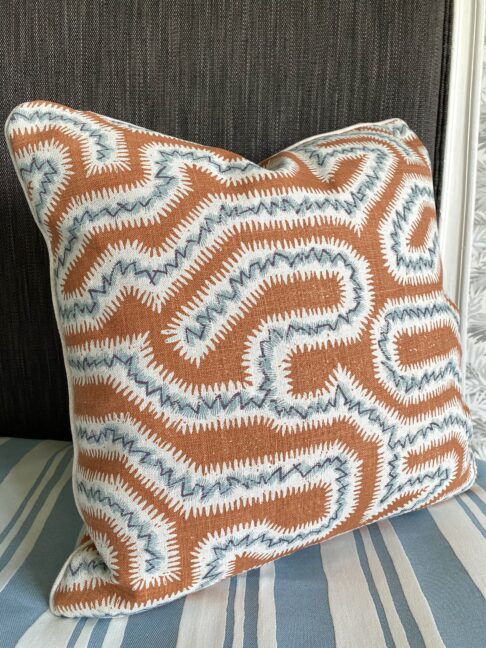 A hand print fabric burnt orange cushion with soft blue accents in a Moorish-inspired, maze-like design on linen.