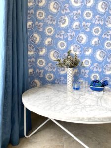 Blue and white floral wallpaper inspired by Russian folk art adorns the wall behind a modern marble coffee table with a vase of flowers.