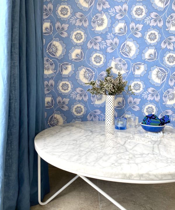 Blue and white floral wallpaper inspired by Russian folk art adorns the wall behind a modern marble coffee table with a vase of flowers.