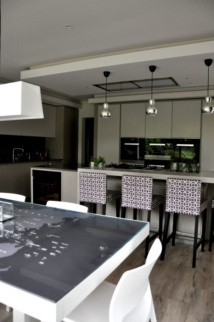 A 'map-under-glass' dining table opposite geometric-print, upholstered bar stools in a modern kitchen.