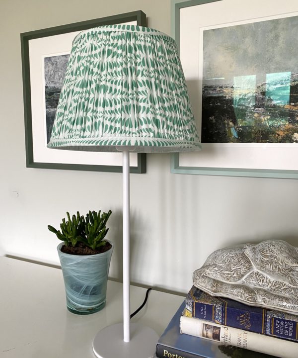 A mint-coloured, block-print lampshade in gathered cotton on a desk with Irish landscape prints in the background.