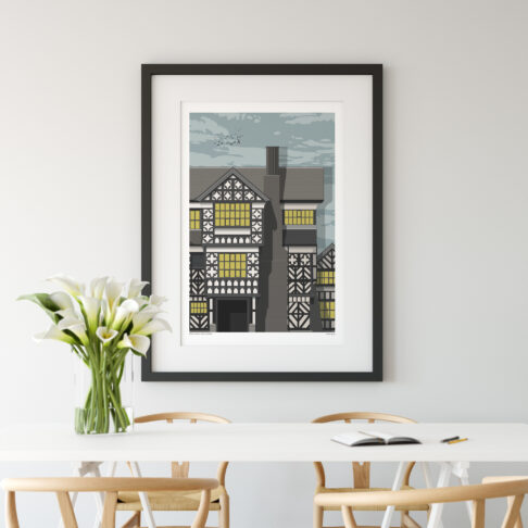 A print of Tudor manor house Little Moreton Hall, Cheshire. The print is hung on a wall in a modern, dining room setting.