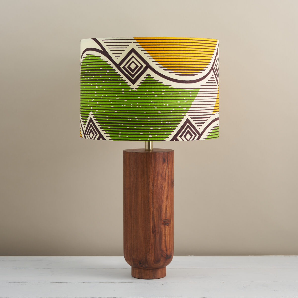 A zingy lime and yellow African print drum shade atop a simple wooden lamp base.