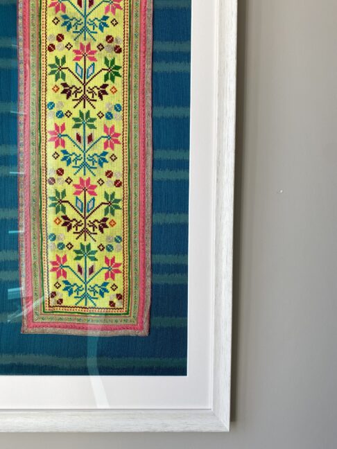 A framed Thai textile against a neutral wall.