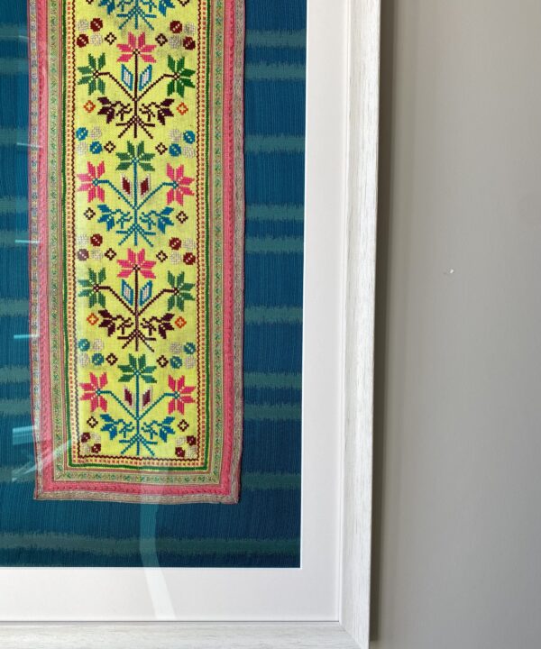 A framed Thai textile against a neutral wall.