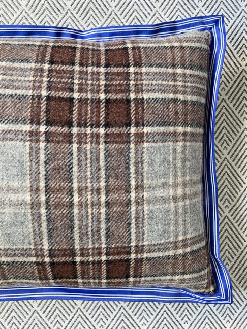 Detail of a brown plaid cushion with a striped blue trim.