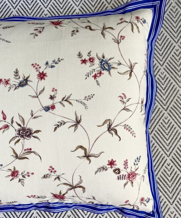 Close-up shot of a floral sprig linen print cushion with a blue striped trim.