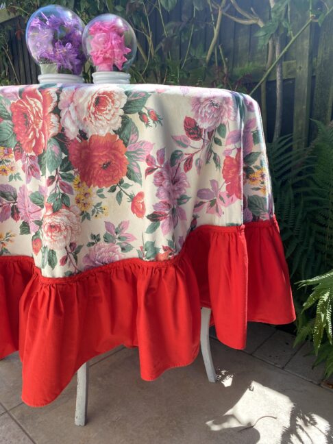 A vintage, floral, circular, skirted tablecloth with a bright, red border.