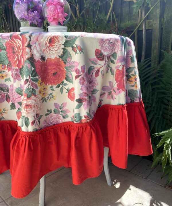 A vintage, floral, circular, skirted tablecloth with a bright, red border.