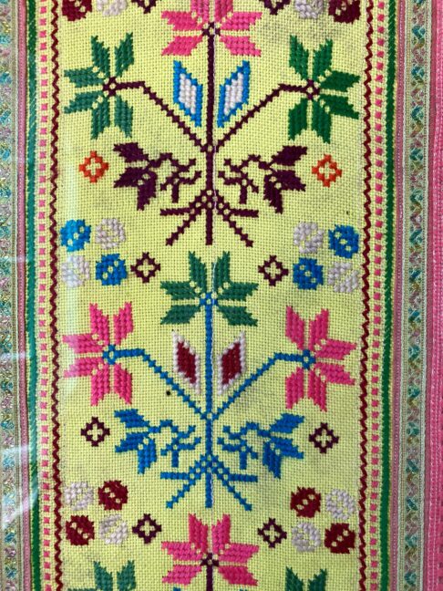 Close up detail of a framed Thai textile in yellow, pink, blue and green.