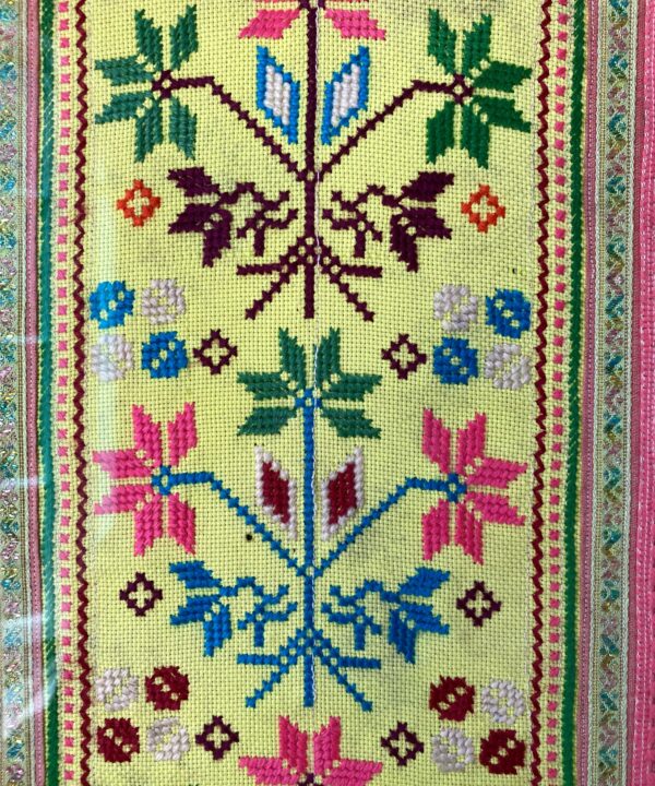 Close up detail of a framed Thai textile in yellow, pink, blue and green.